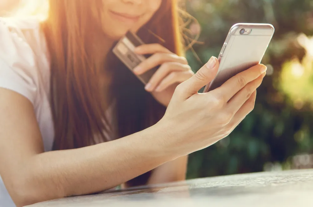 menina olhando para o celular com um cartão de crédito na mão