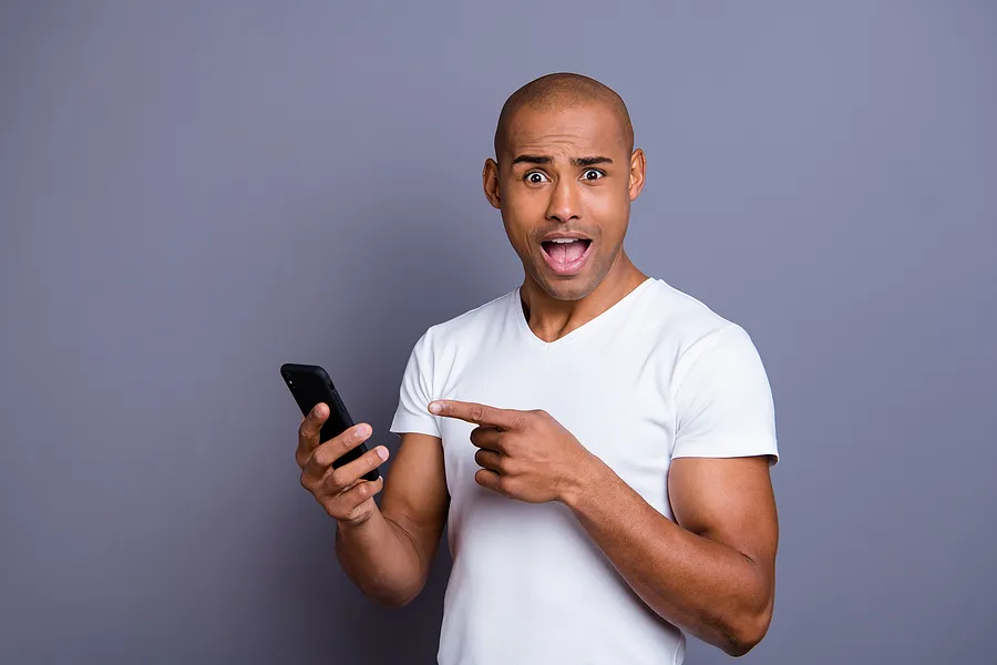 Homem segurando um celular, com expressão de surpresa