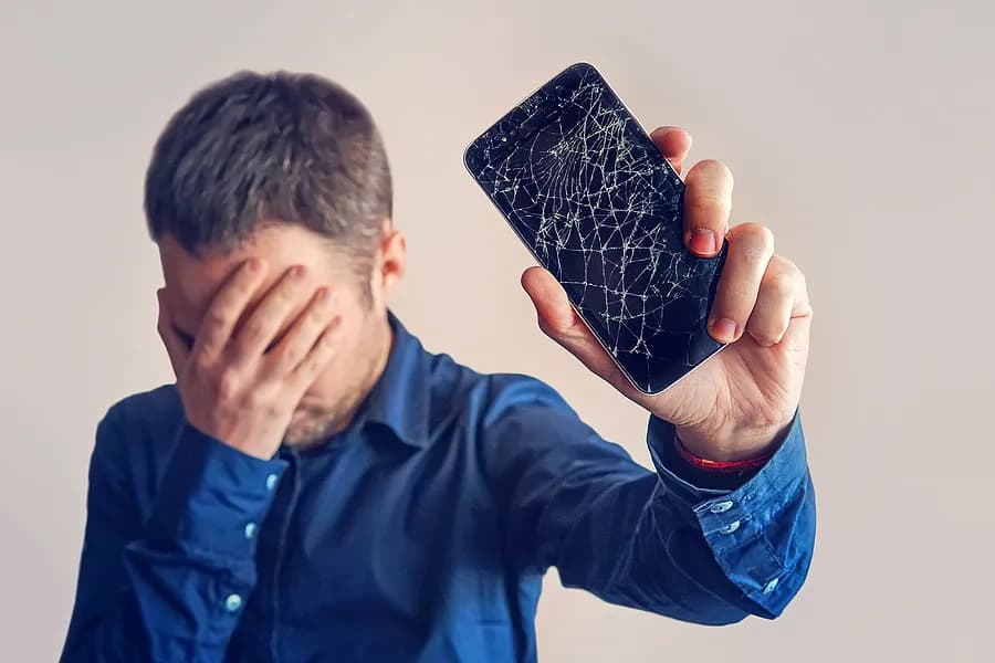 Um homem cobrindo os olhos e segurando um celular afastado do corpo.