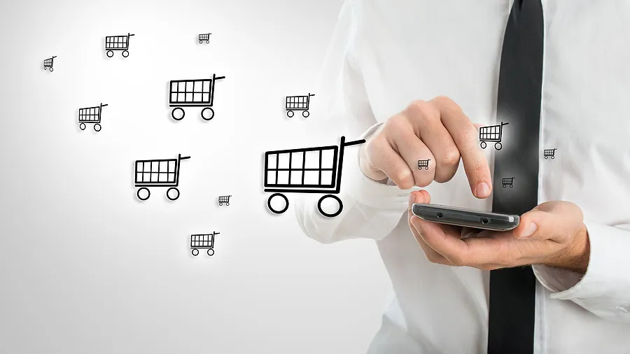 Empresário usando um smartphone com ícones de carrinho de compras, simbolizando o comércio eletrônico móvel e as compras de celulares pela internet.