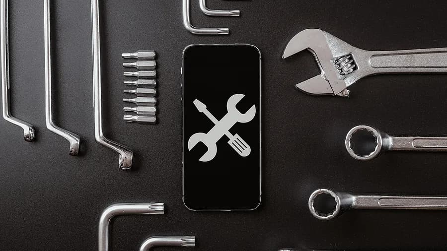 Ferramentas de diagnóstico e conceito de reparo de smartphones, com a tela do celular exibindo ícones de chave inglesa e chave de fenda rodeados por ferramentas de metal.