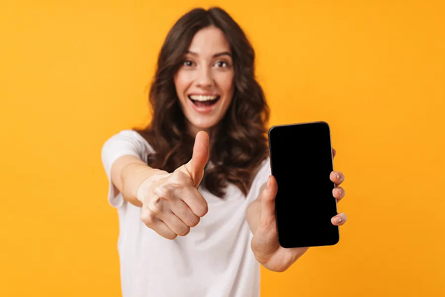 Mulher sorridente segurando um smartphone e mostrando o polegar para cima, simbolizando o sucesso do processo de verificação e certificação do telefone.