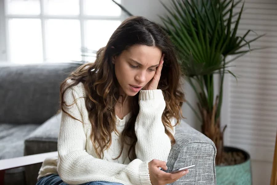 Mulher preocupada olhando para seu smartphone, representando a importância de verificar os relatórios de telefones usados e compreender o histórico do aparelho antes de comprá-lo.