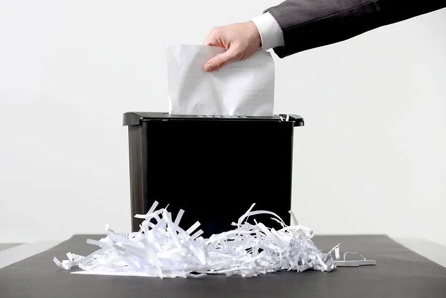 Colocação manual de documentos em uma trituradora de papel, ilustrando a destruição certificada de dados e o descarte seguro de informações confidenciais.